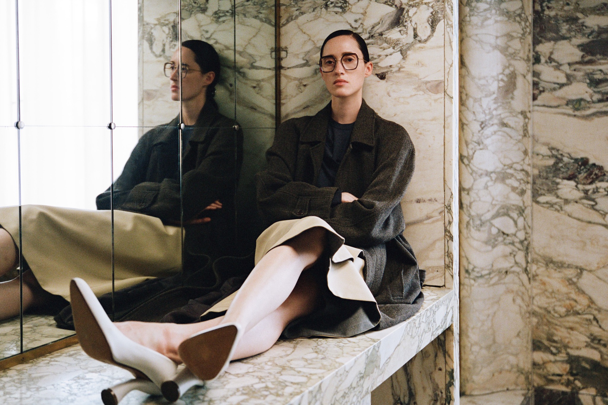 Woman in glasses is sitting near the mirror